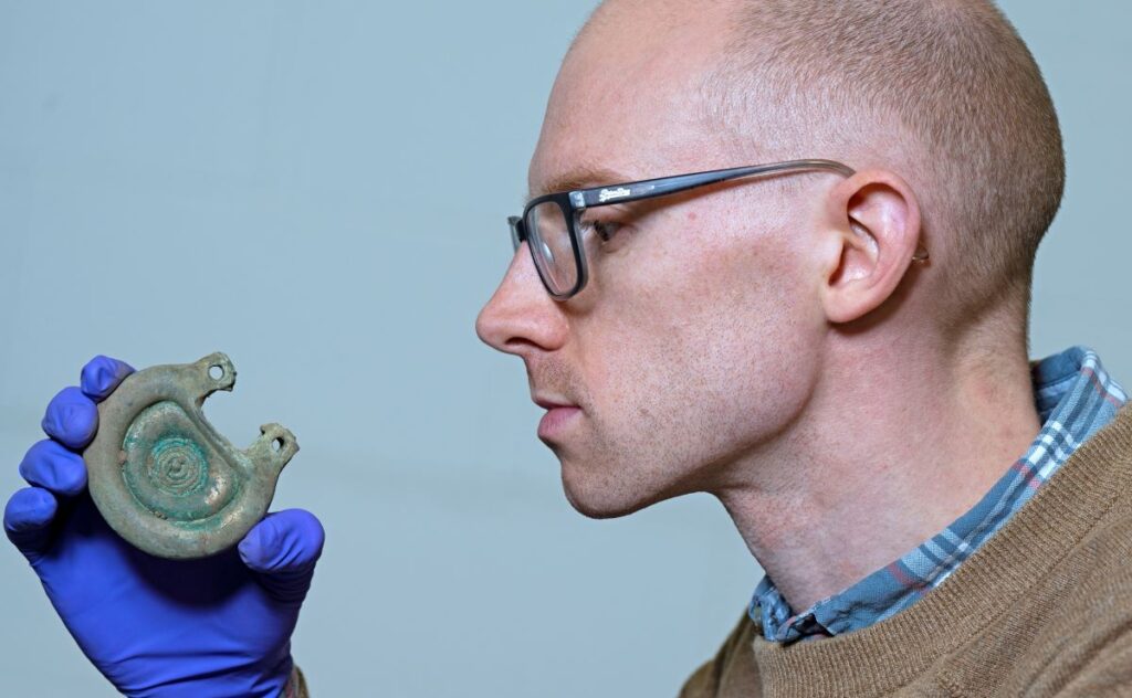 Curator Dr Matthew Knight examining a bronze object from the Peebles Hoard. Credit: Neil Hanna.