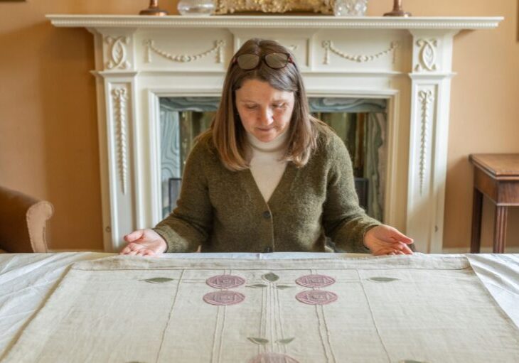 Curator Emma Inglis with a Jane Younger bedcover with an embroidered panel in the Glasgow Style from the Hill House. Credit Phil Wilkinson